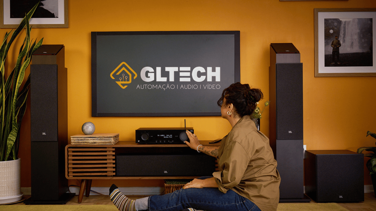 Mulher ajusta sistema de áudio em sala com automação GLTECH, mostrando integração de som, vídeo e controle inteligente.